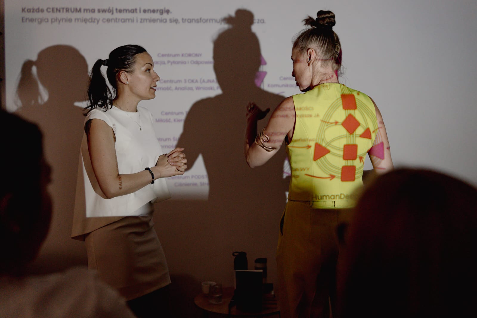 Alina Gwoździewicz w kamizelce z wykresem Human Design pracująca z uczestniczką na warsztacie
